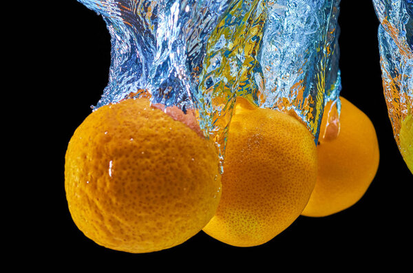 Fresh orange, mandarine falling in water with splash on black background