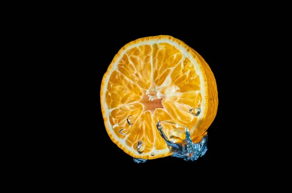 Свежий апельсин падает в воду с брызгами на черном фоне — стоковое фото