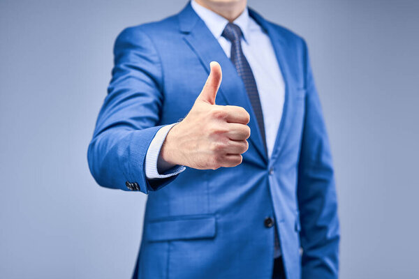 Бизнесмен в синем костюме на серо-голубом фоне держит перед собой руку в знак одобрения. Рука с большим пальцем вверх. Концепция утверждения решения
.