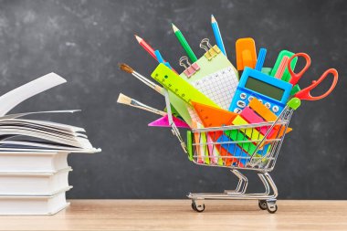 Okul için çeşitli ofis gereçleri bir el arabasında ve tahta bir masa üzerinde ders kitapları. Okul hazırlığı kavramı, yeni bir okul yılının başlangıcı..