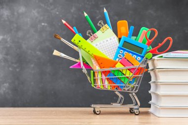 Okul için çeşitli ofis gereçleri bir el arabasında ve tahta bir masa üzerinde ders kitapları. Okul hazırlığı kavramı, yeni bir okul yılının başlangıcı..