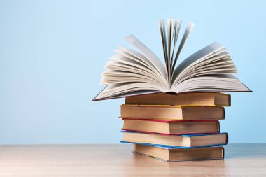 Açık bir kitap, açık mavi bir duvara karşı ahşap bir masanın üzerinde duran bir yığın kitabın üzerinde duruyor.