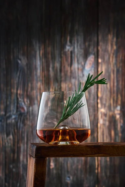 古い木製の壁に対してカウンターの上にウイスキーとローズマリーの小枝のショットを持つ結晶ガラス 低キー — ストック写真
