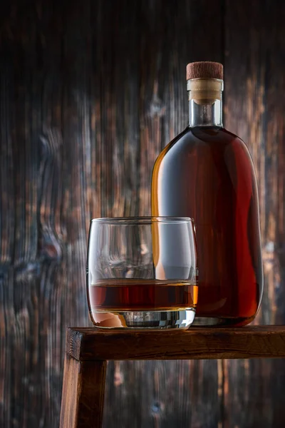 古い木製の壁に対して カウンターの上にウイスキーとウイスキーの完全なボトルの一部を持つ丸いガラス 低キー — ストック写真