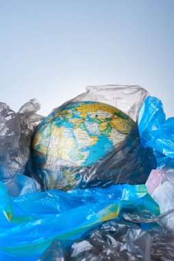 Dünyayı plastik atıklardan koruma, çevre kirliliğiyle mücadele kavramı, dünya hafif bir arkaplanda çeşitli çöp yerleşimlerinin bulunduğu bir yığının içinde yatıyor. Poşet yok.