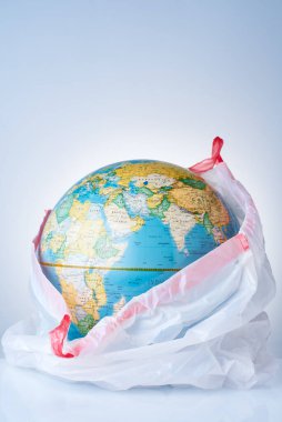Dünyayı plastik atıklardan koruma kavramı, çevre kirliliğiyle mücadele, çevre için mücadele, beyaz bir çöp torbasında hafif bir arka planda bir dünya. Poşet yok.