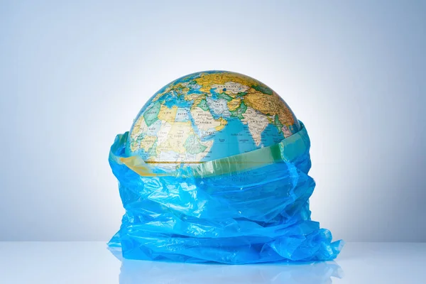 The concept of protecting the world from plastic waste, fighting environmental pollution, fighting for the environment, a globe in a blue garbage bag on a light background. No plastic bags.