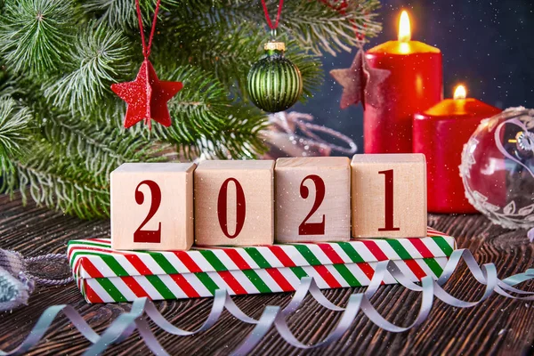 stock image Cubes with numbers 2021 on a Christmas background with gifts in boxes, decorated with a spruce branch and lit candles. New year's background with free space for text.