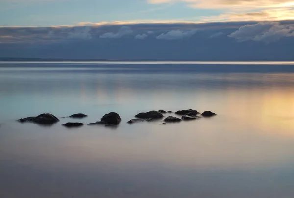 dawn on smooth water and dark stones in the distance