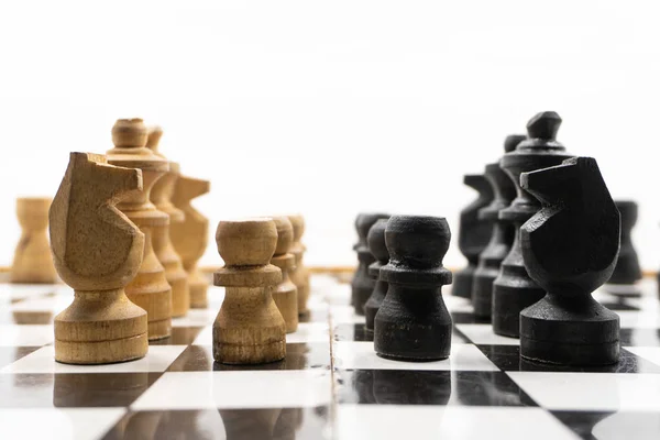 two sides of black and white chess pieces, which are made of wood, are facing each other. There is a white background for placing posts