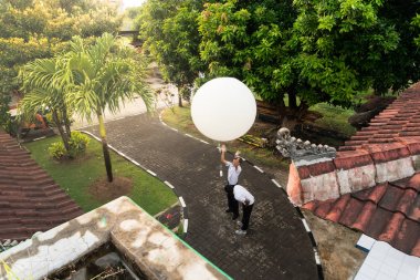BADUNG/BALI-APRIL 10 2019: An observer at Ngurah Rai Meteorological station releasing the big white radio sonde balloon to measure the lability of the atmosphere clipart