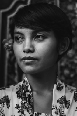 Siyah beyaz tek renkli güzel kısa saçlı Asyalı Balili bir kadının eski bir portresi. Çiçekli kumaş giyer ve kulağına çiçek takar.