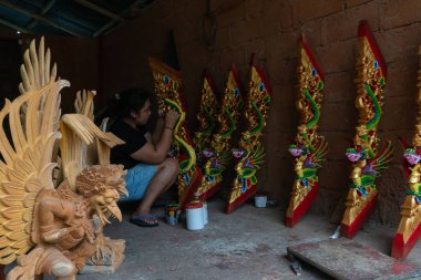 Ubud/Endonezya-Nisan 27 2019: Ubud'lu bir kadın zanaatkar, parlak ve çekici renkler kullanarak ejderha oyma ve boyama yapıyor. Ubud Bali el sanatları üreticilerinden biridir