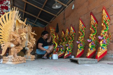 Ubud/Endonezya-Nisan 27 2019: Ubud'lu bir kadın zanaatkar, parlak ve çekici renkler kullanarak ejderha oyma ve boyama yapıyor. Ubud Bali el sanatları üreticilerinden biridir