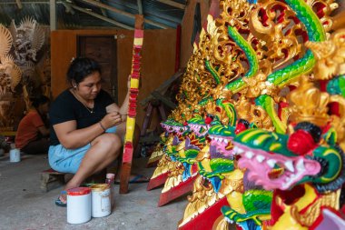 Ubud/Endonezya-Nisan 27 2019: Ubud'lu bir kadın zanaatkar, parlak ve çekici renkler kullanarak ejderha oyma ve boyama yapıyor. Ubud Bali el sanatları üreticilerinden biridir