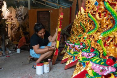 Ubud/Endonezya-Nisan 27 2019: Ubud'lu bir kadın zanaatkar, parlak ve çekici renkler kullanarak ejderha oyma ve boyama yapıyor. Ubud Bali el sanatları üreticilerinden biridir