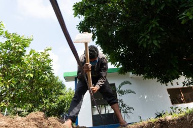 Bir işçi bahçede çapa kullanarak çukur kazıyor.