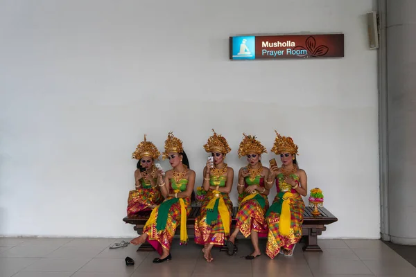 BALI / INDONESIA-APRIL 30 2019: πέντε γυναίκες χορεύτριες από το Μπαλί κάθονταν αναπαυόμενες σε μακριές καρέκλες μετά την παράσταση στη σκηνή. Μιλούν μεταξύ τους και χρησιμοποιούν τα κινητά τους για σέλφι και κουβεντούλα. — Φωτογραφία Αρχείου