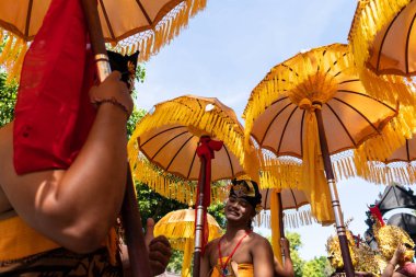Denpasar/Endonezya-15 Haziran 2019: Tapınak festivali sırasında Hindu tören geçit töreninde geleneksel renkli şemsiyeler ile etnik kostümlü Balili dansçı grubu. Bali halkı kültürü