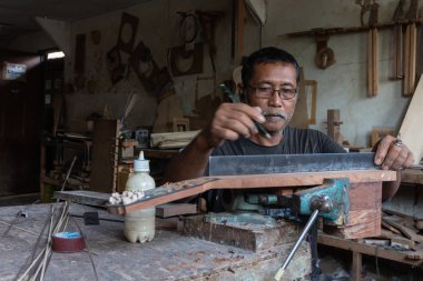Gianyar,Bali/Endonezya-30 Mayıs 2019: Guwang Village, Gianyar, Bali'de I Wayan Tuges'e ait ahşap gitar atölyesinde bir gitar ustası ölçüyor ve hassas bir gitar parçası olduğundan emin oluyor.