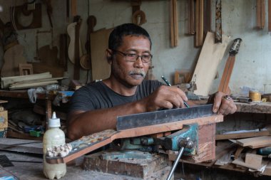 Gianyar,Bali/Endonezya-30 Mayıs 2019: Guwang Village, Gianyar, Bali'de I Wayan Tuges'e ait ahşap gitar atölyesinde bir gitar ustası ölçüyor ve hassas bir gitar parçası olduğundan emin oluyor.