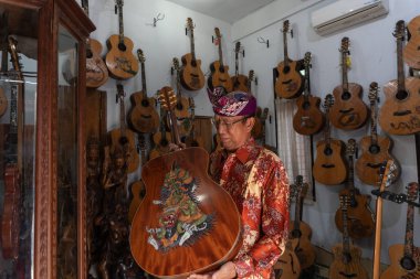 Gianyar,Bali/Endonezya-30 Mayıs 2019: Guwang'da Tuges ve Blueberry oyma gitarsahibi Wayan Tuges, Gianyar Bali, duvara asılan oyma gitarlarıyla