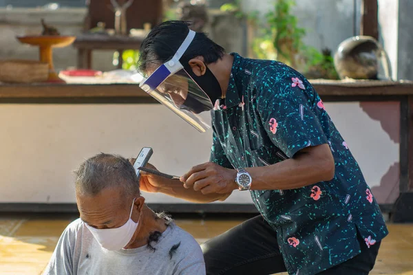 Bir berber ev işi yapıyor. COVID-19 salgını birçok işletmenin kapanmasına neden oldu. Ayakta kalmak için, girişimciler müşterilere gitmeyi tercih ederler. Yeni normal yaşam için sağlık protokollerine bağlı kal.