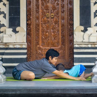 Covid-19 salgını sırasında çocuklarla yoga yapmak eğlenceli ve bağışıklığı artıran etkinliklerden biridir. Tipik bir Bali binasında ahşap oymalarla yoga yapıyorlar.