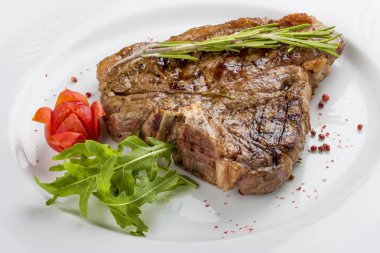 Yeşillik ile biftek T-kemik. Beyaz bir plaka üzerinde.