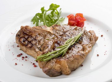 Yeşillik ile biftek T-kemik. Beyaz bir plaka üzerinde.