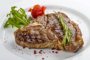 Yeşillik ile biftek T-kemik. Beyaz bir plaka üzerinde.