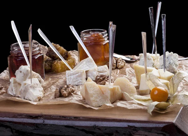 A set of cheeses on a wooden board with honey and jam — Stock Photo, Image