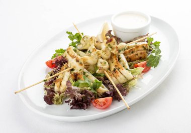 Şişlerde ızgarada salata ve soslu kalamar. Beyaz arka planda