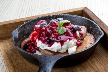 Beyaz arka planda bir tavada kahvaltı. Kremalı ve reçelli krep. Tahta tepside.