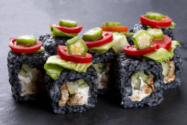 Siyah arka planda domatesli siyah pirinçli suşi rulosu.