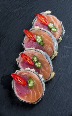 Somon balıklı suşi rulosu ve siyah arka planda ton balığı.