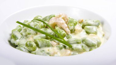 Beyaz arka planda ıspanaklı ve karidesli patates gnocchi.