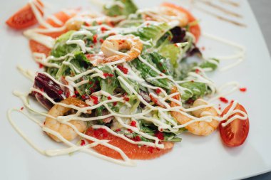 Salata karidesleri, Somon dilimleri, domatesler, masada bir plaka üzerinde yeşillik