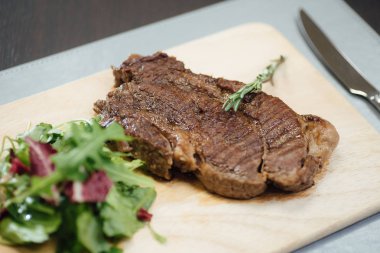 Masada bir tahta kesme tahtasında kızarmış et ve yeşillikler bir parça