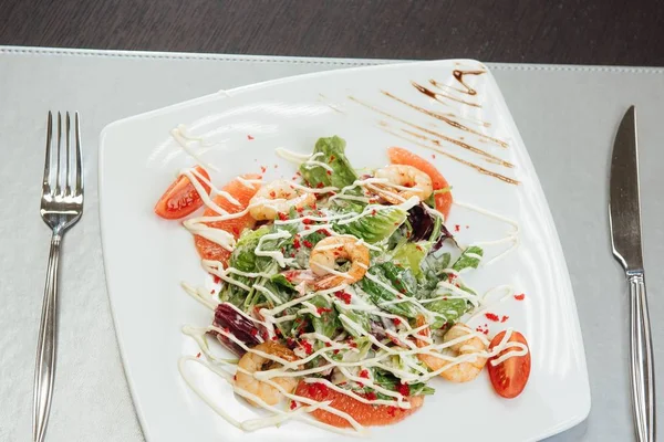 Salata karidesleri, Somon dilimleri, domatesler, masada bir plaka üzerinde yeşillik