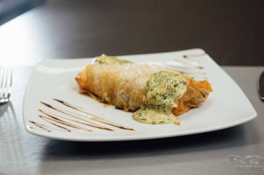 Masada beyaz bir tabak üzerinde beyaz sos ile kızarmış et