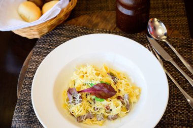 Bir plaka üzerinde eritilmiş peynir ve et parçaları ile makarna