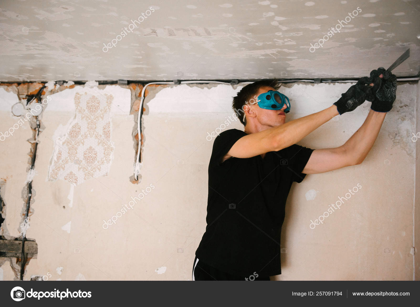 A Man Removes Old Paint From The Ceiling With A Spatula