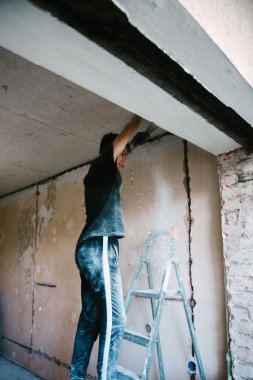 Bir adam bir spatula ile tavana eski boya kaldırır