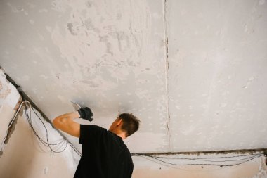 Bir adam bir spatula ile tavana eski boya kaldırır