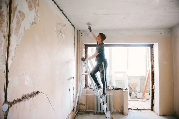 stock image A man removes old paint from the ceiling with a spatula