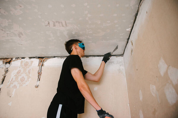 A man removes old paint from the ceiling with a spatula