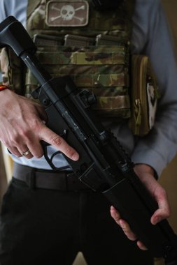 Takım elbiseli ve vücut zırhı giymiş bir adam elinde makineli tüfek tutuyor..