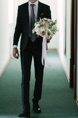 Takım elbiseli bir adam yakın bir yerde bir çiçek buketi tutar..