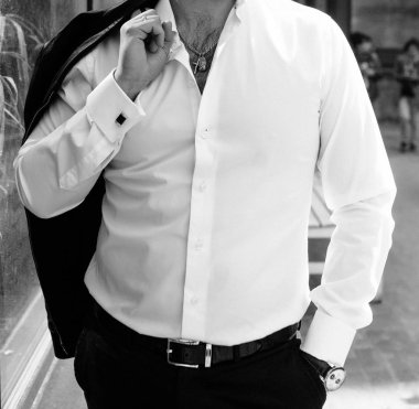 Beyaz gömlekli bir adam eliyle ceketini arkasında tutar..
